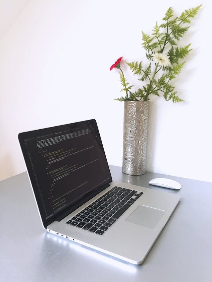 about-01 Laptop with programming code on screen beside a vase with flowers, creating a modern workspace.
