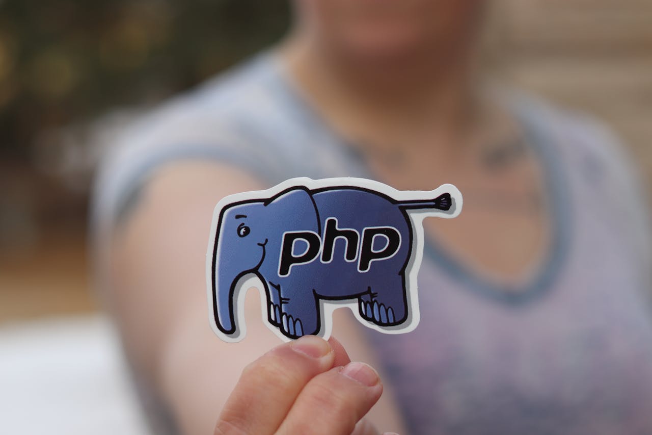hero-img-02 A woman's hand holding a PHP elephant mascot sticker, blurred background.